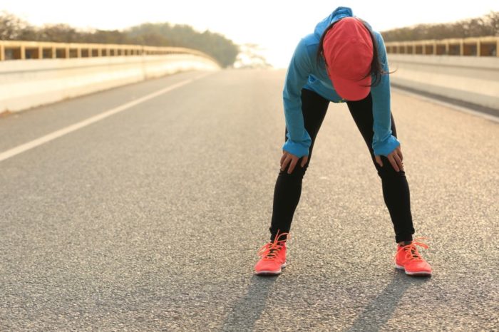 A woman bent over with her hands on her knees after a long run. 