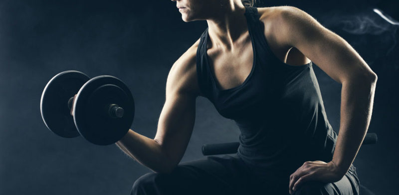 Woman doing a seated bicep curl in a dark studio